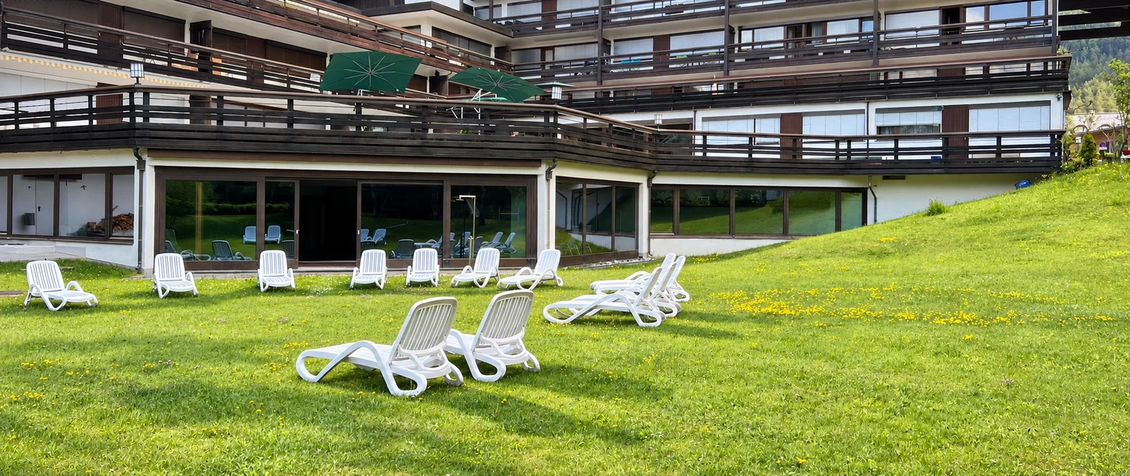 Garten des Appartementhauses Birkenwald mit grüner Liegewiese und weißen Liegestühlen