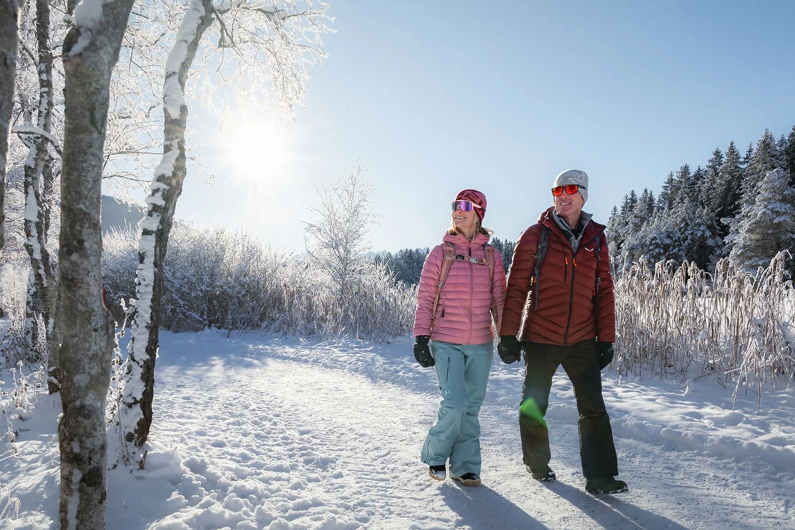 Winterwandern in der Region Seefeld_Mann und Frau laufen morgens beim Wildsee_Aufnahme gegen die Sonne