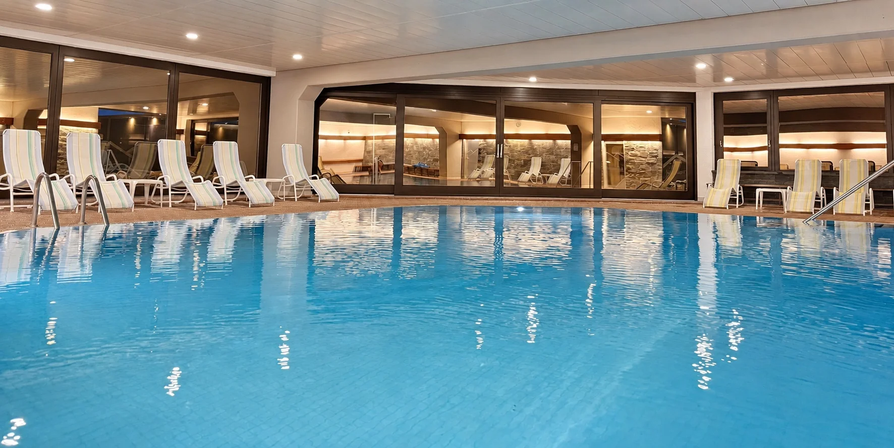 Blick über das Schwimmbad mit Liegestühlen und warmer Beleuchtung im Appartementhaus Birkenwald